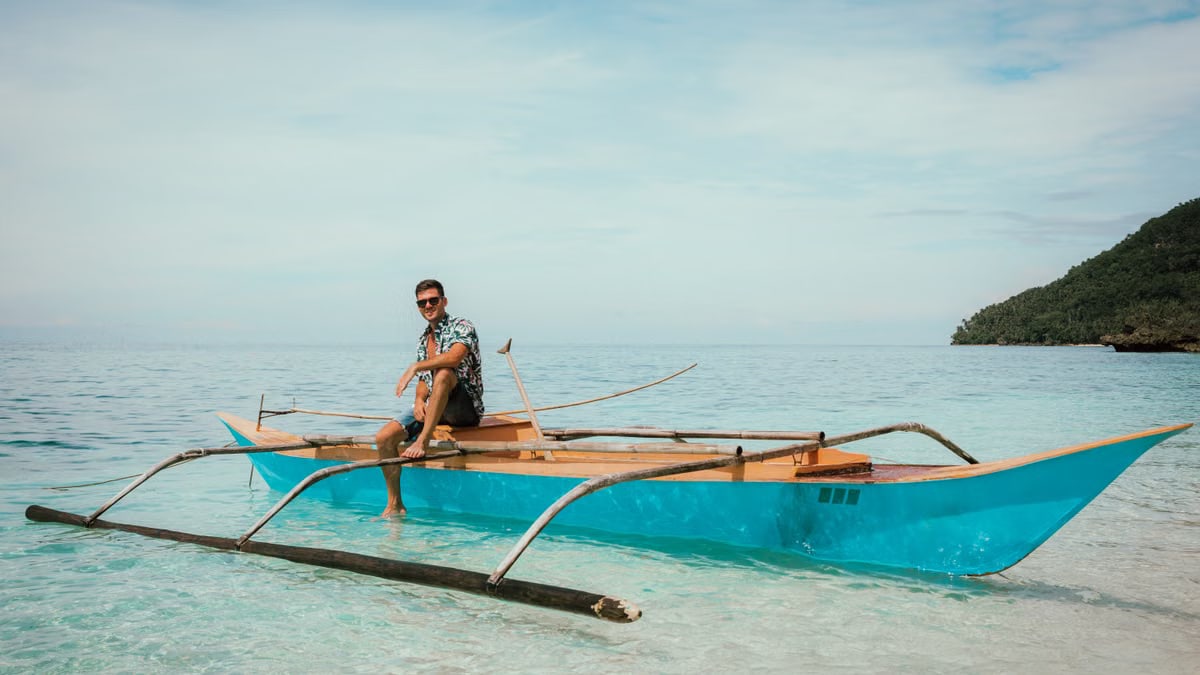 Relaxed man sitting on wooden vessel and relaxing against cloudy blue sky in sea